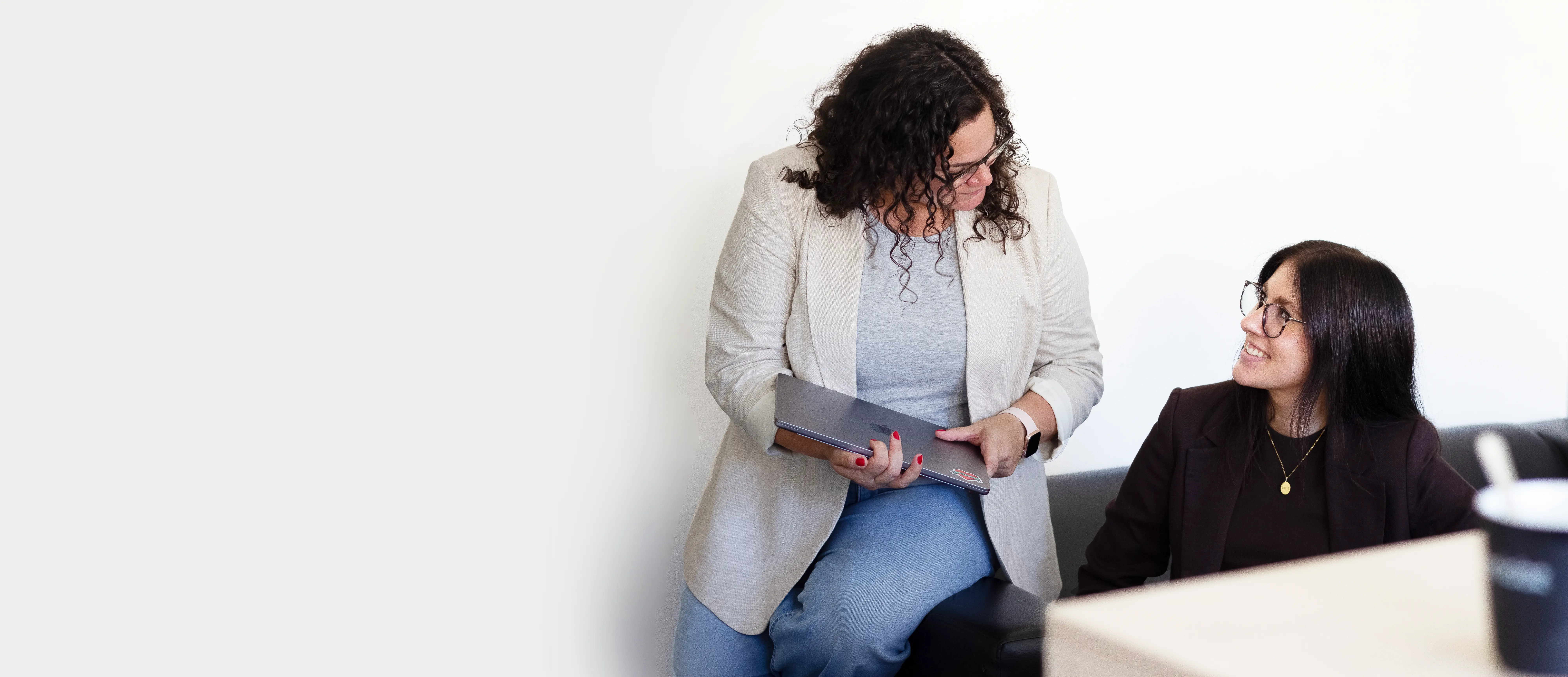 Foto von zwei lächelnden Frauen im Büro, eine mit Laptop in der Hand