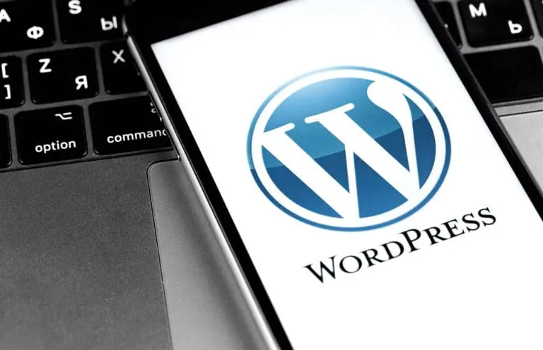 Nahaufnahme eines Smartphones mit dem WordPress-Logo auf dem Bildschirm vor einer Laptop-Tastatur mit kyrillischen und lateinischen Buchstaben