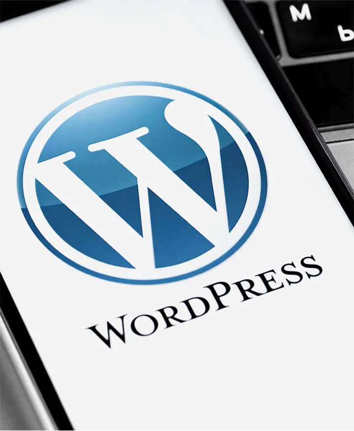 Smartphone-Bildschirm zeigt das WordPress-Logo, im Hintergrund eine Laptop-Tastatur