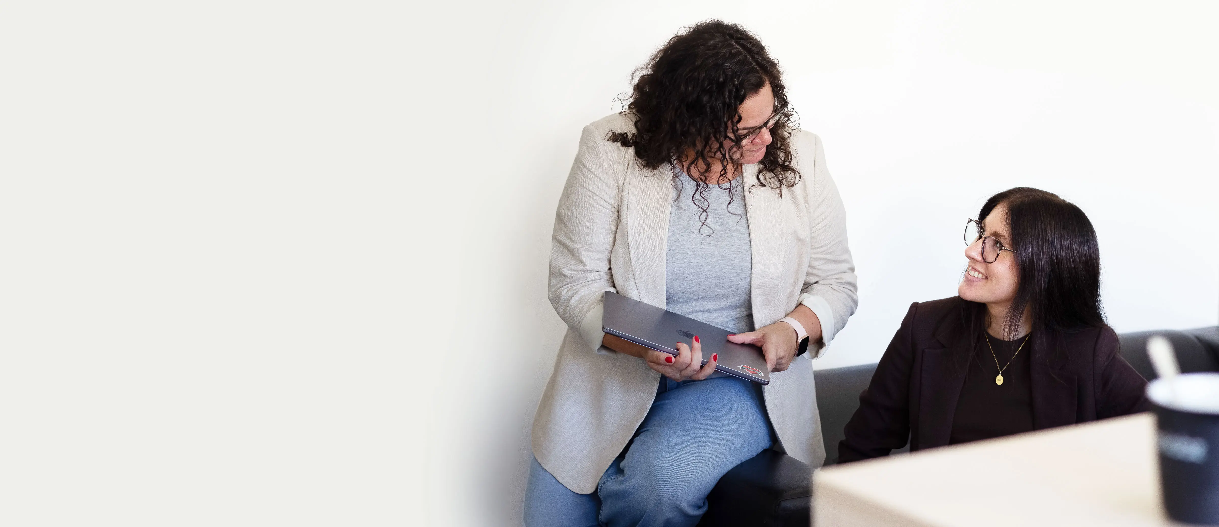 Foto von zwei lächelnden Frauen im Büro, eine mit Laptop in der Hand
